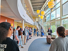 Students at Orientation standing in a semicircle in the School of Music lobby, listening to the Dean of Music speak.