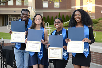 Four Smart Tranfer graduates holding their certificates, smiling for the camera. 