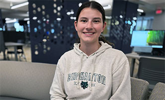 Grace Van Baaren in a Binghamton University sweatshirt, sitting in Begley Learning Commons.