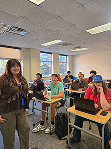Students seated in a classroom at desks, instructor stands at the front of the room.