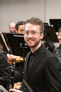 Student in black attire holding a clarinet, on stage with other musicians.