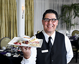 Student in a vest and tie, standing in the Casola Dining Room, holding a professionally plated meal.