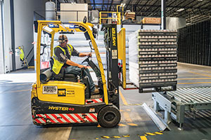 In a warehouse, person driving a forklift loaded with pallets.