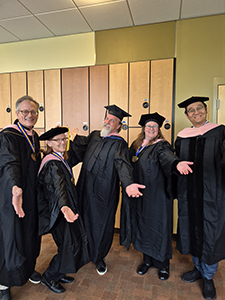School of Music faculty in their caps and gowns, extending their arms in a welcoming fashion.