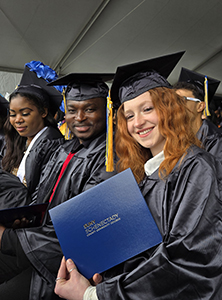 Two graduates in caps and gowns, seated under the tent at Commencement.