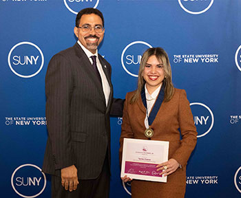 EOP student Yarisa Cueva stand with SUNY Chancellor King in front of a blue SUNY backdrop.