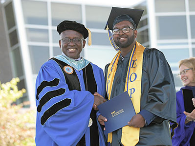 EOP graduate in cap and gown, shaking hands with Dr. Steady Moono at commencement.