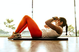 Woman in athletic wear, laying on a yoga mat, doing crunches.