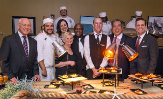 Campus members, community members, donors standing at a table of food at a fundraising event on campus.