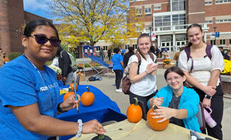 Students gather around a table and a large poster for an upcoming theater performance.