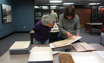 Adult students working in a library, leaning over a book together.