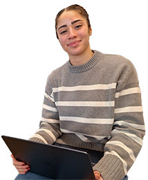 Female with dark hair that is pulled back, wearing a gray and white stiped sweater, holding an open laptop. 