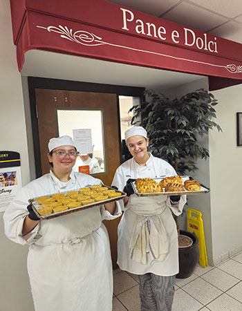Culinary student holding trays of bakery treats in front of Pane e Dolci.
