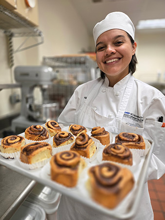 Culinary student holding a tray of freshly-baked cinnamon rolls. 