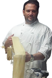 Chef Armondo Cioccke wearing a white chef coat, holding a sheet of freshing pressed pasta.