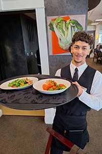 HCAT student in the Casola Dining Room, holding a serving tray with two salads.