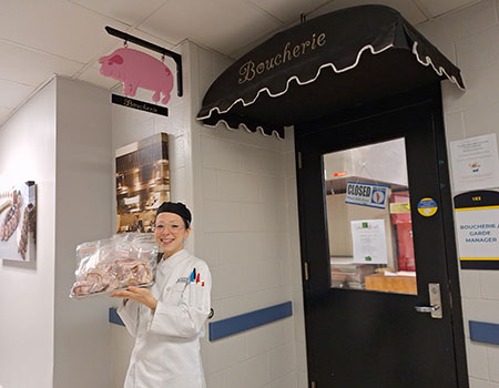Faculty member Rain O'Donnell holding meat that is for sale in front of the Boucherie entrance.
