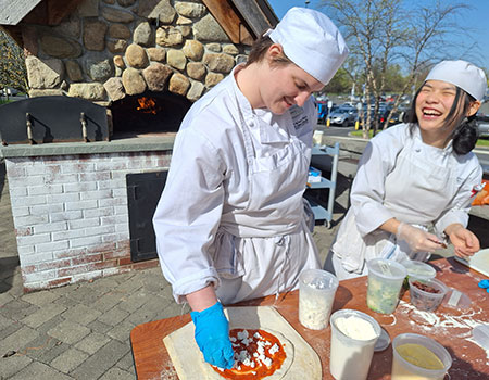 Two culinary student making pizzas to cook in the brick oven.