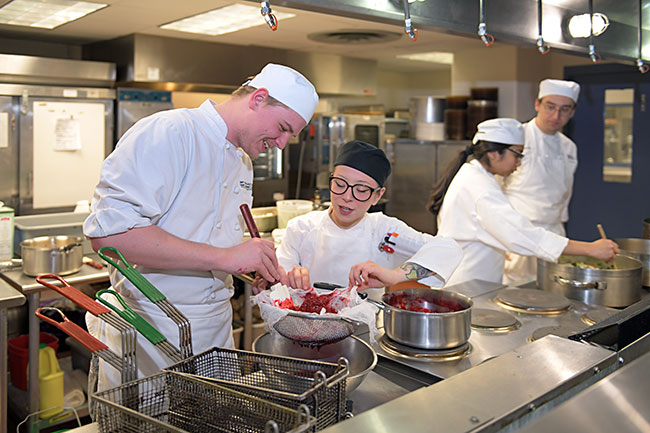 Culinary Arts students working around a stove with a professor in a hot food lab.