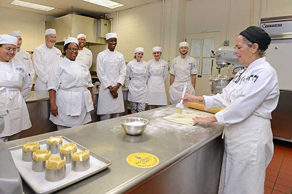 Baking professor demonstrating over dough to a room of students.