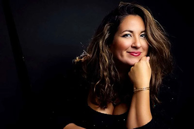 Nicole Zuraitis in a dark shirt sitting in front of a dark background.
