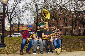 Members of the Trojan Horns Brass Band sitting on a park bench, holding their instruments. 