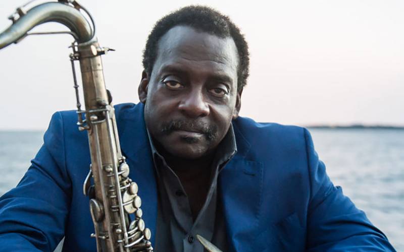 David Murry in a blue suit, black shirt, holding a saxophone.