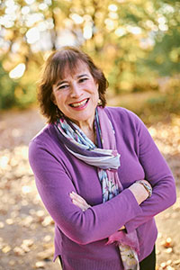 Gail Wein in a purple shirt and patterned purple scarf, standing outside in autumn.