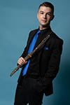 Matthew Ross in a dark suit, blue tie, holding his flute.