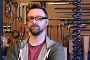 Chris Cromer, owner of A Minor Tune Up, standing in front of a peg board full of tools. 