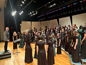 Choral members in formal dress on stage with a conductor.