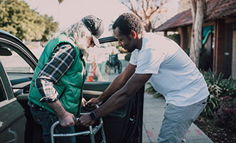 Health aide assisting a man with a walker getting out of a car.