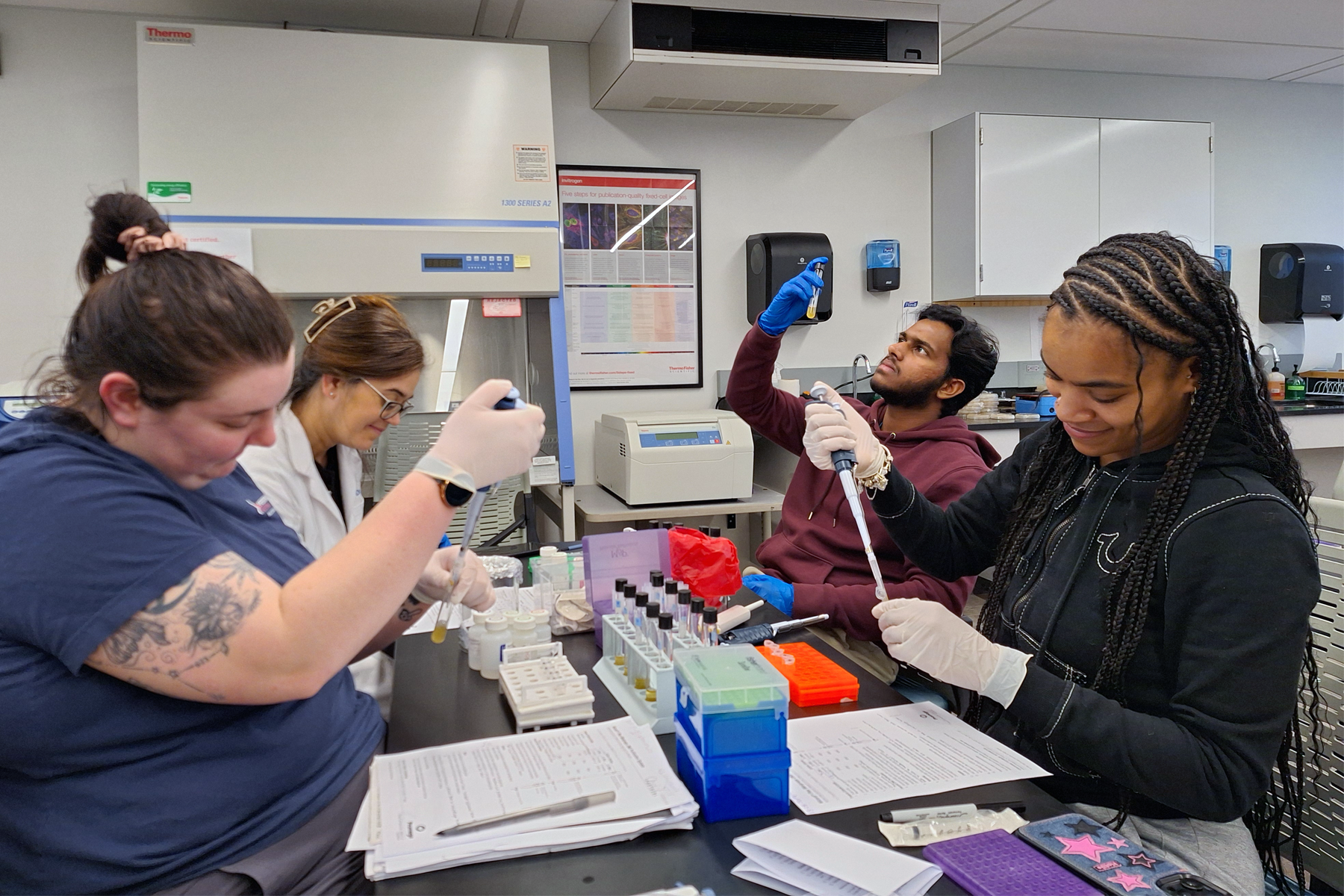 Students and professor using Biotech equipment, seated at table in Biotechnology Facility