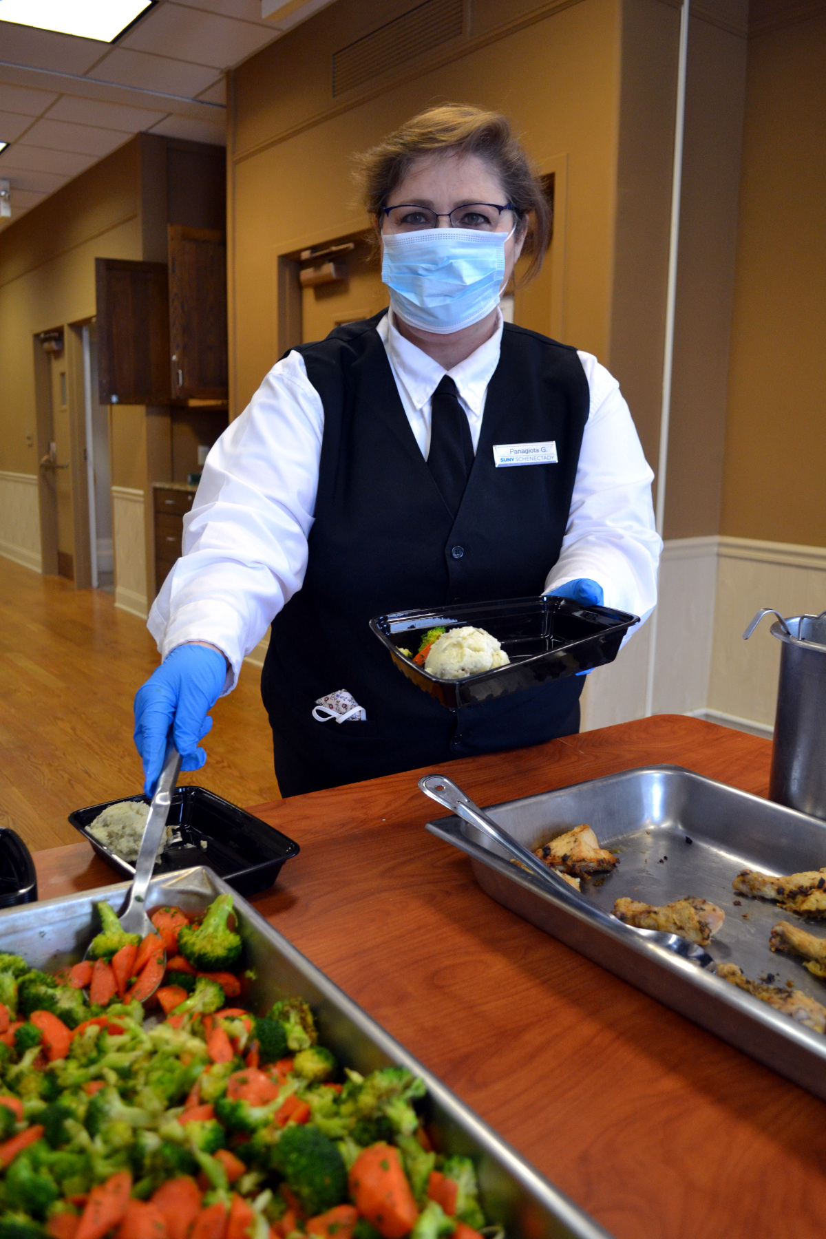 Hospitality student in uniform putting vegetables into a container for a prepared meal.