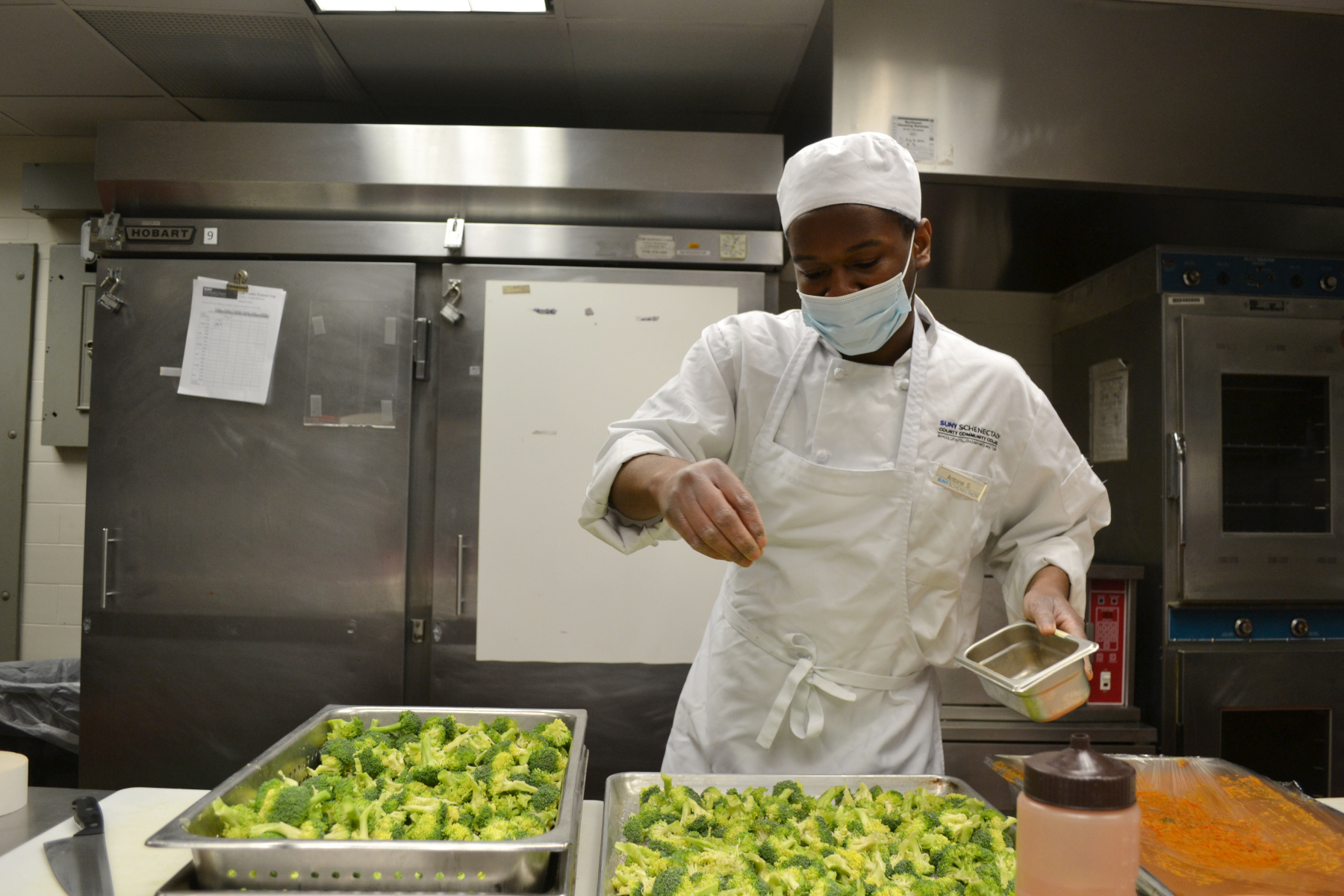 Student Chef pouring salt on broccoli, in Culinary lab