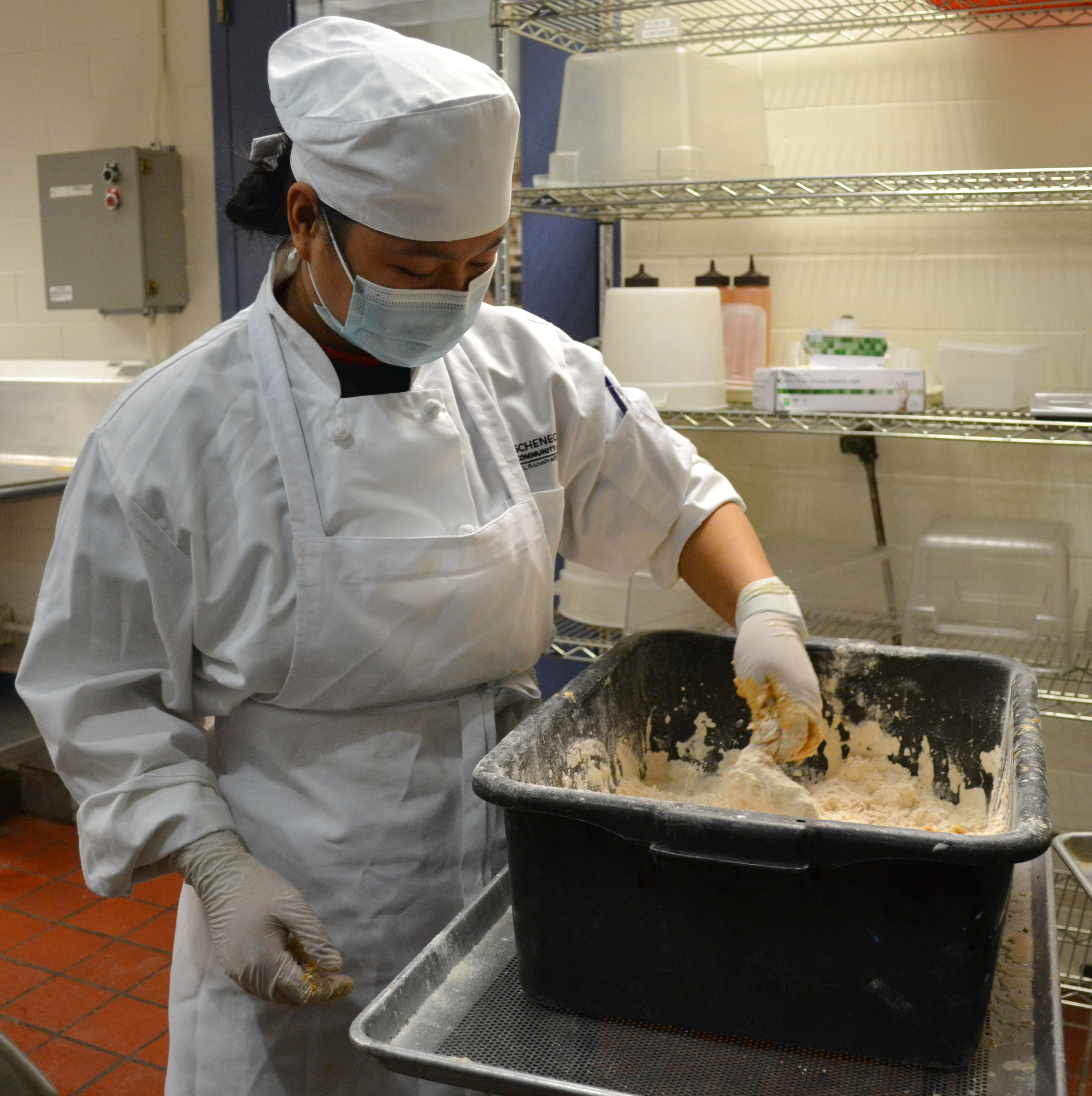 Student chef putting batter on chicken.