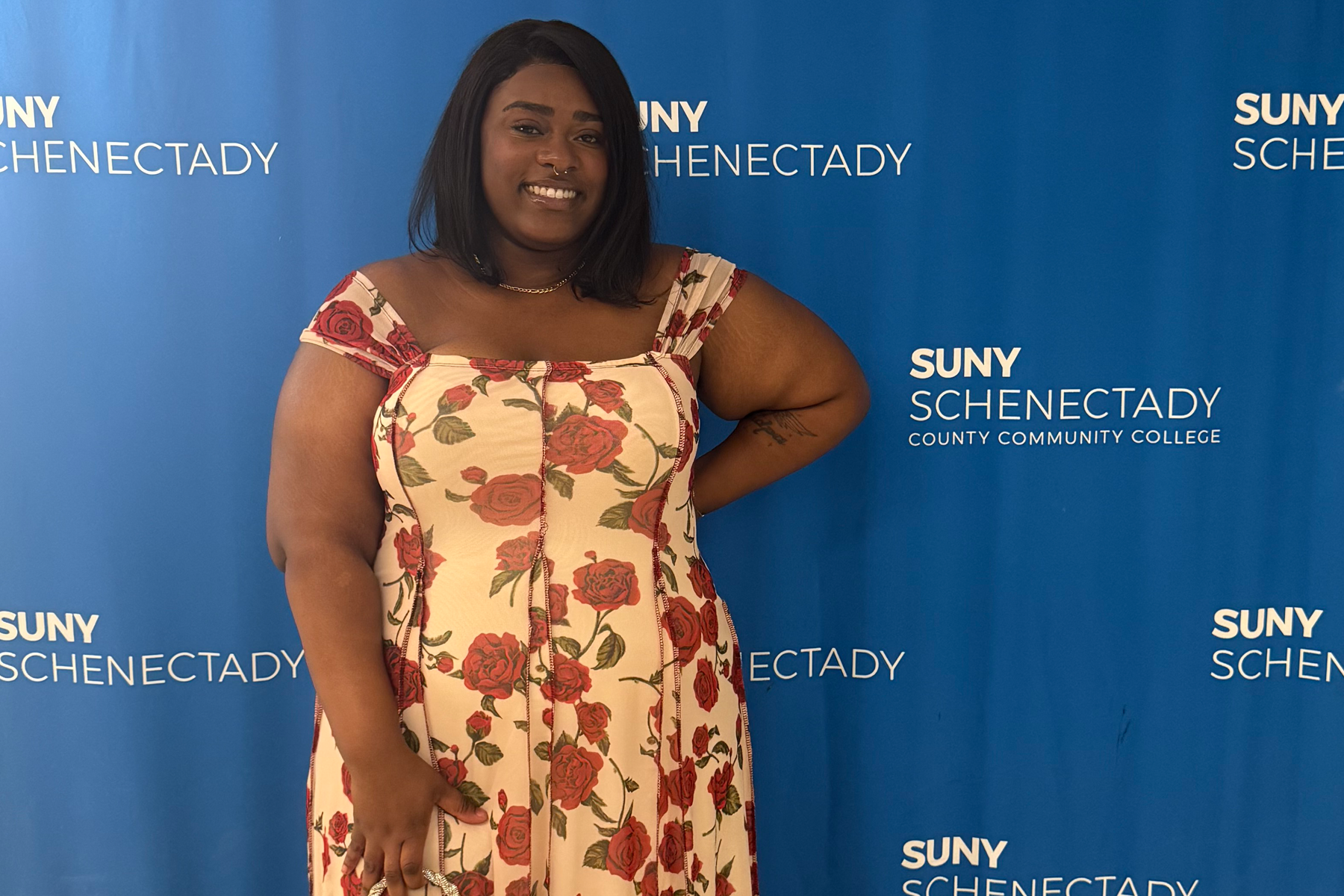 Imani Romain-Barthley wearing floral dress, smiling, in frong of College backdrop