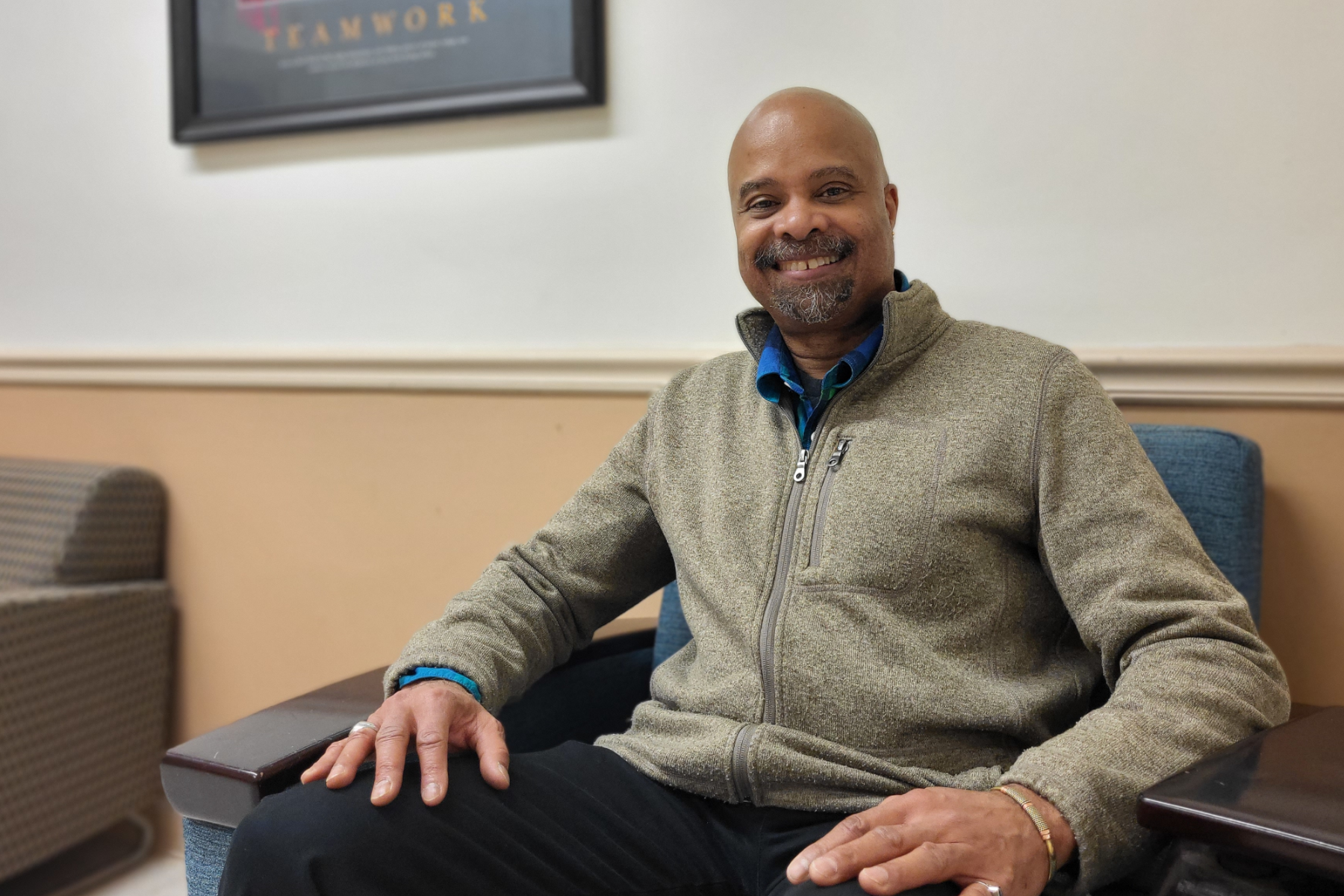 Stephen Tyson seated, smiling, in hallway outside of art classroom